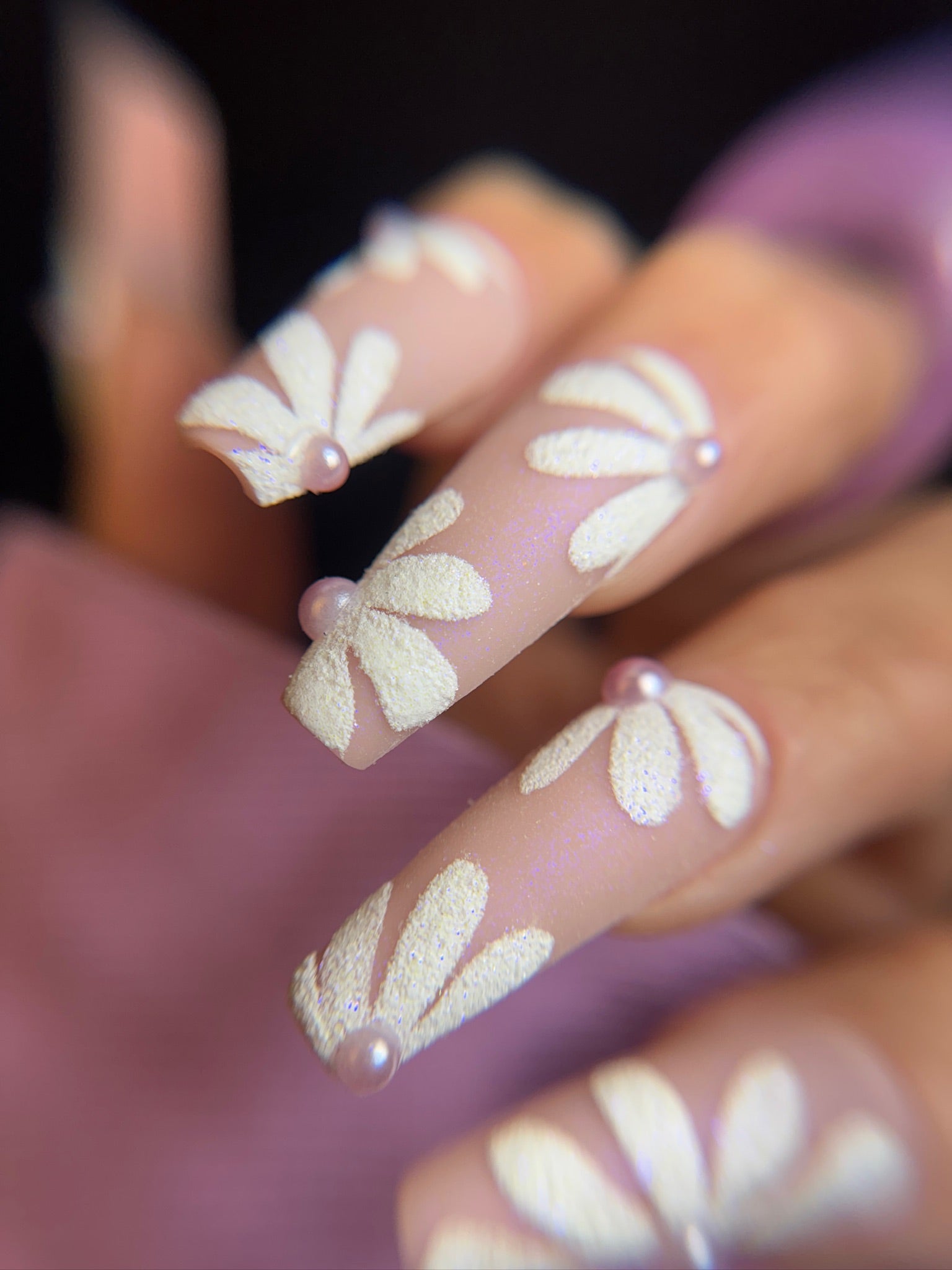 Nails with floral design and small pearls on a blurred background