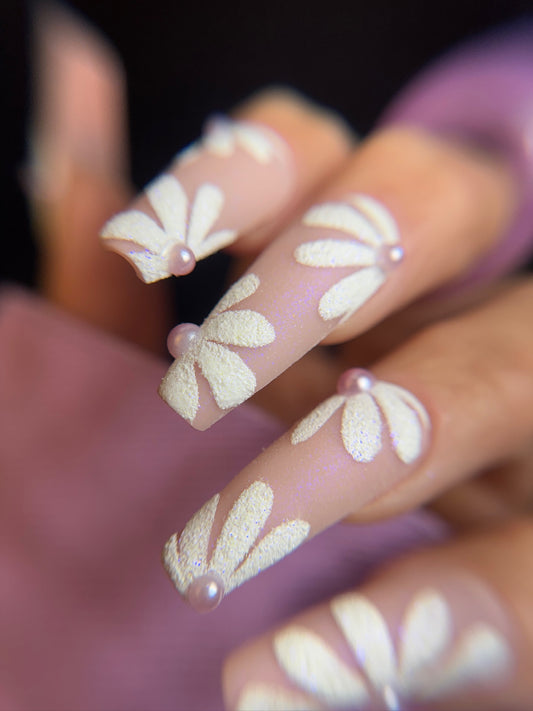 Nails with floral design and small pearls on a blurred background