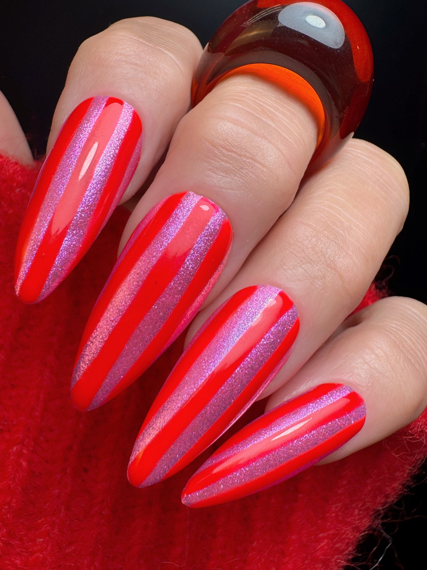 Close-up of a hand with red and pink striped nails against a red background