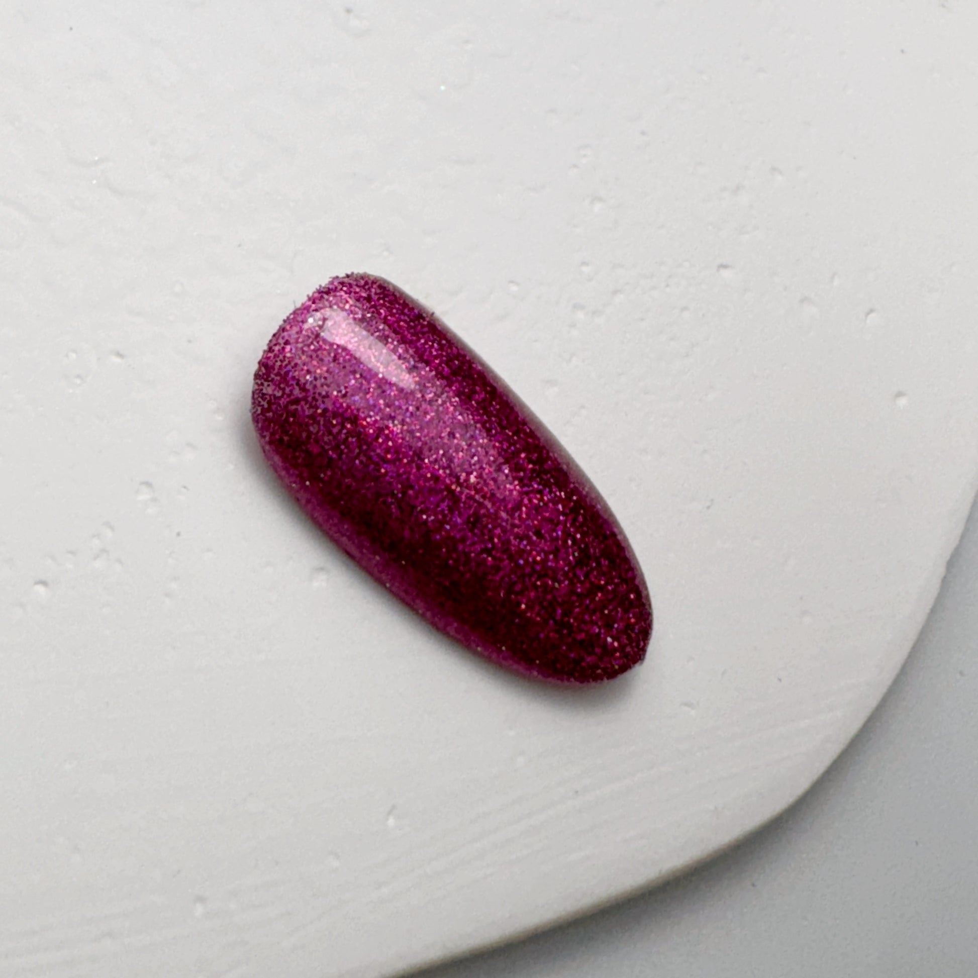 Nail tip with glittery finish on white textured surface.