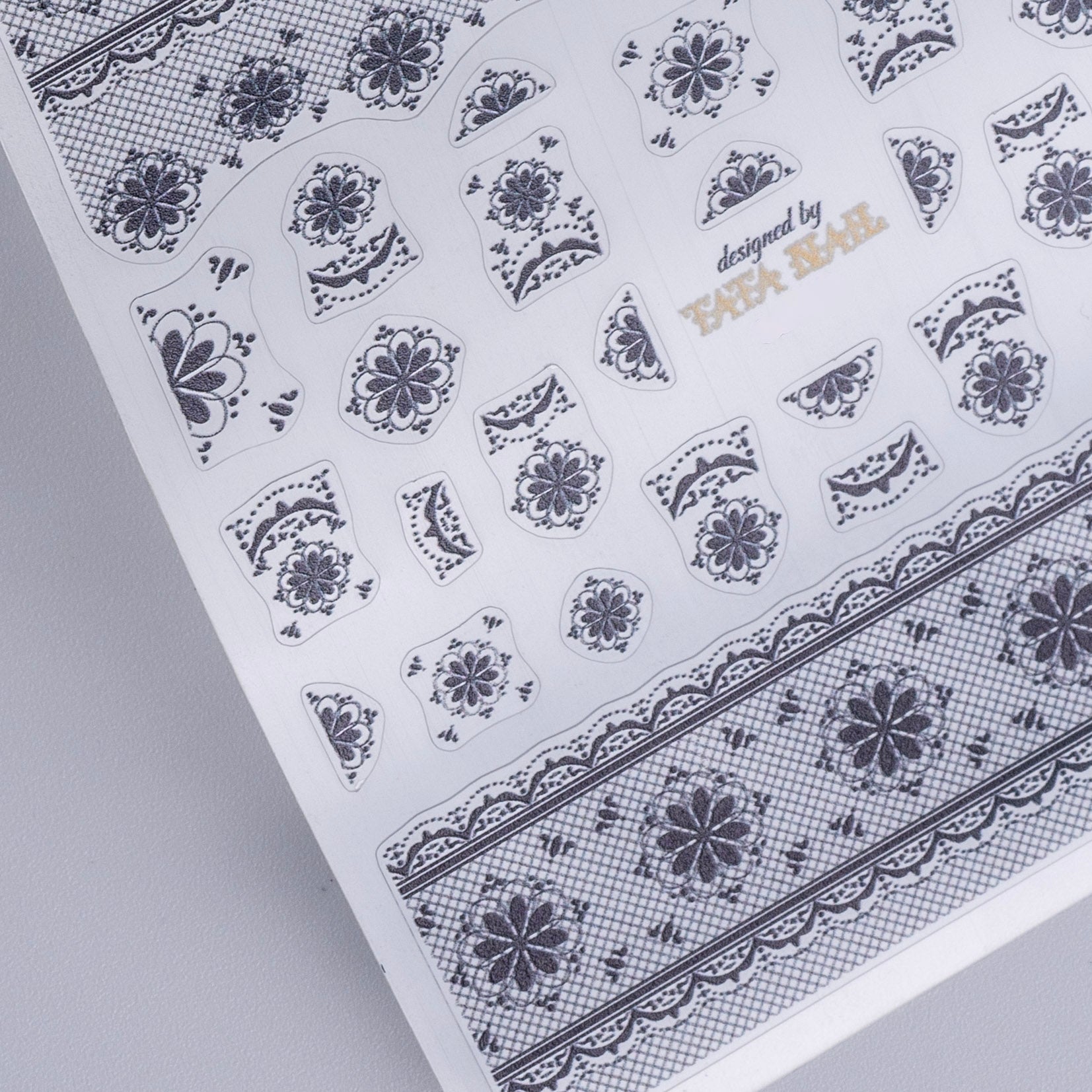Sheet of floral nail art stickers with 'designed by TATA Nail' text on a gray background