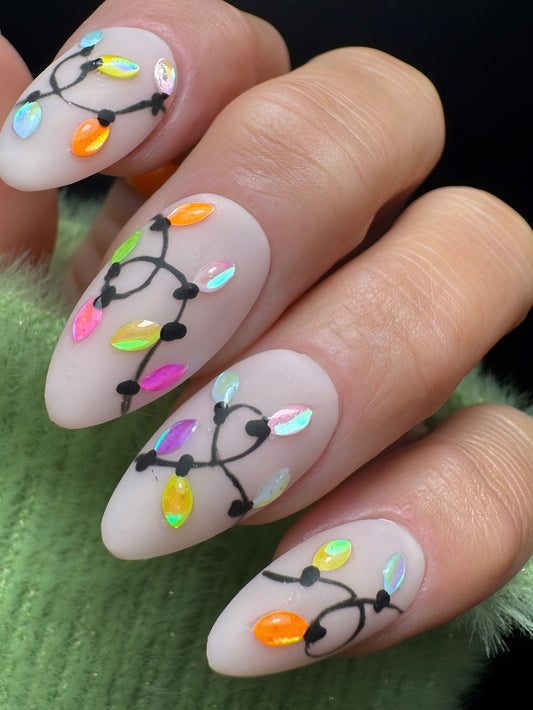 Nails with festive light bulb design on a green fabric background