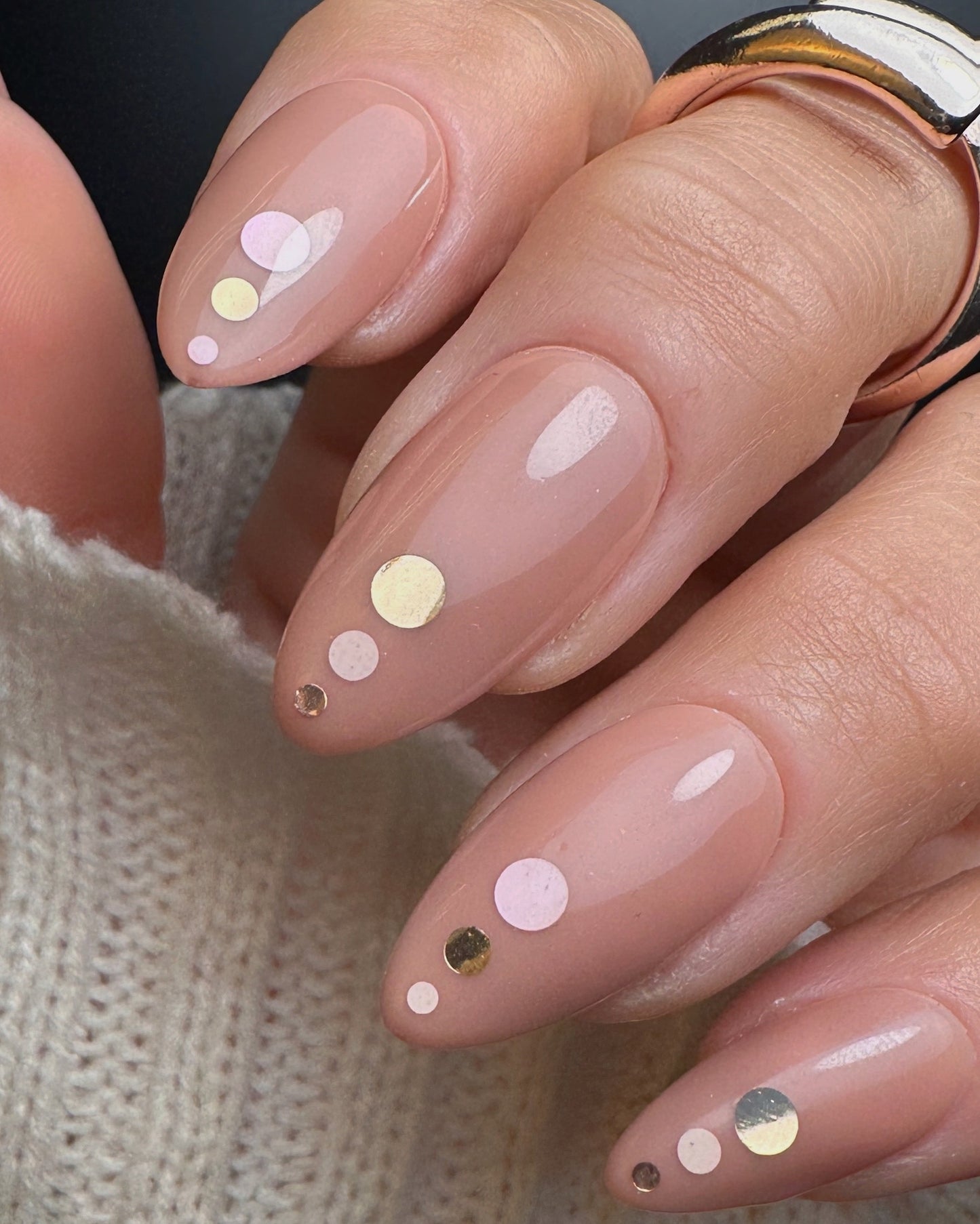 Nails with a nude polish and decorative dots on a neutral background