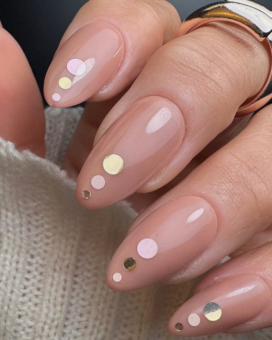 Nails with a nude polish and decorative dots on a neutral background