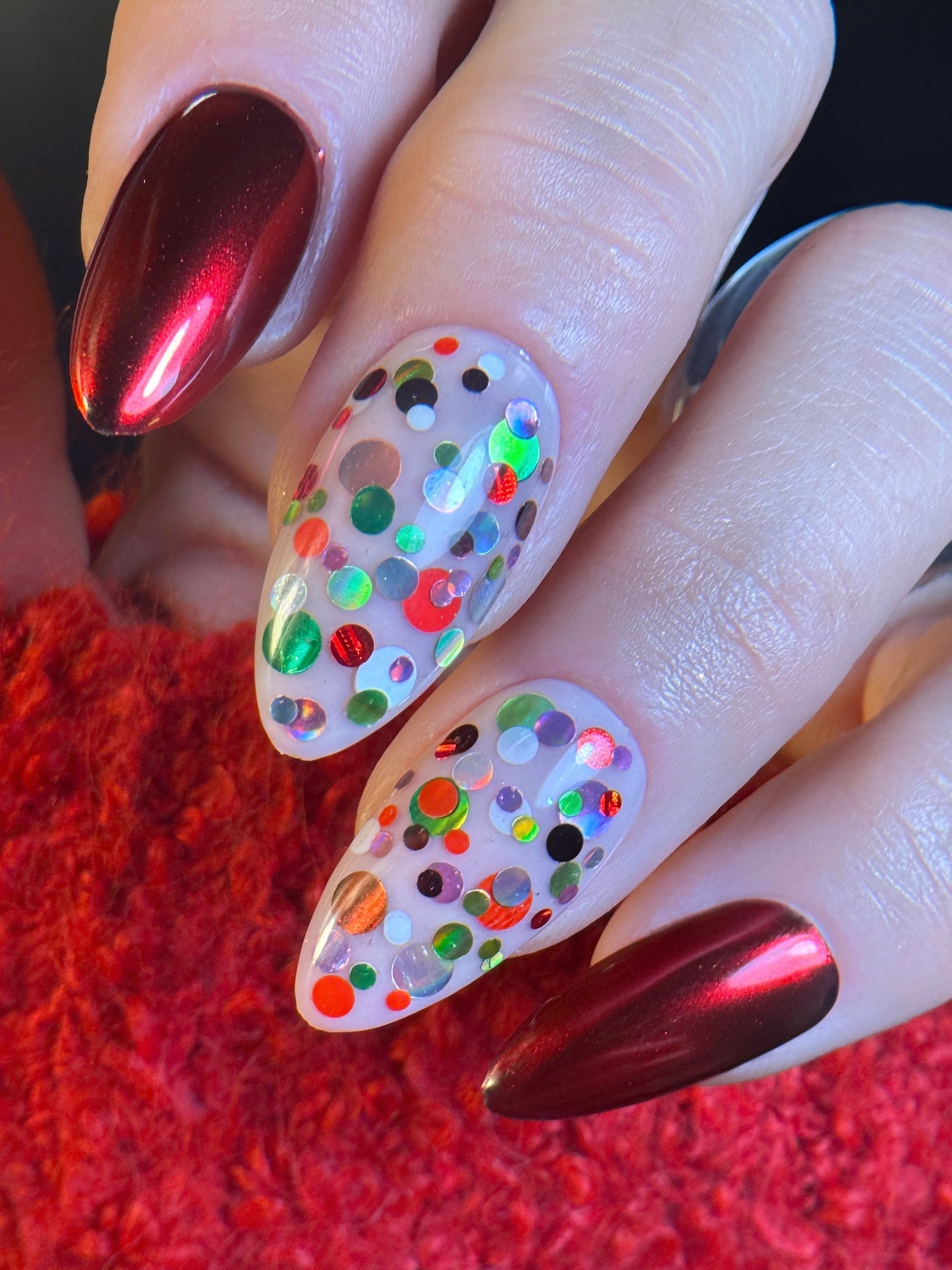 Nails with colorful dot design and red metallic polish on a red textured background