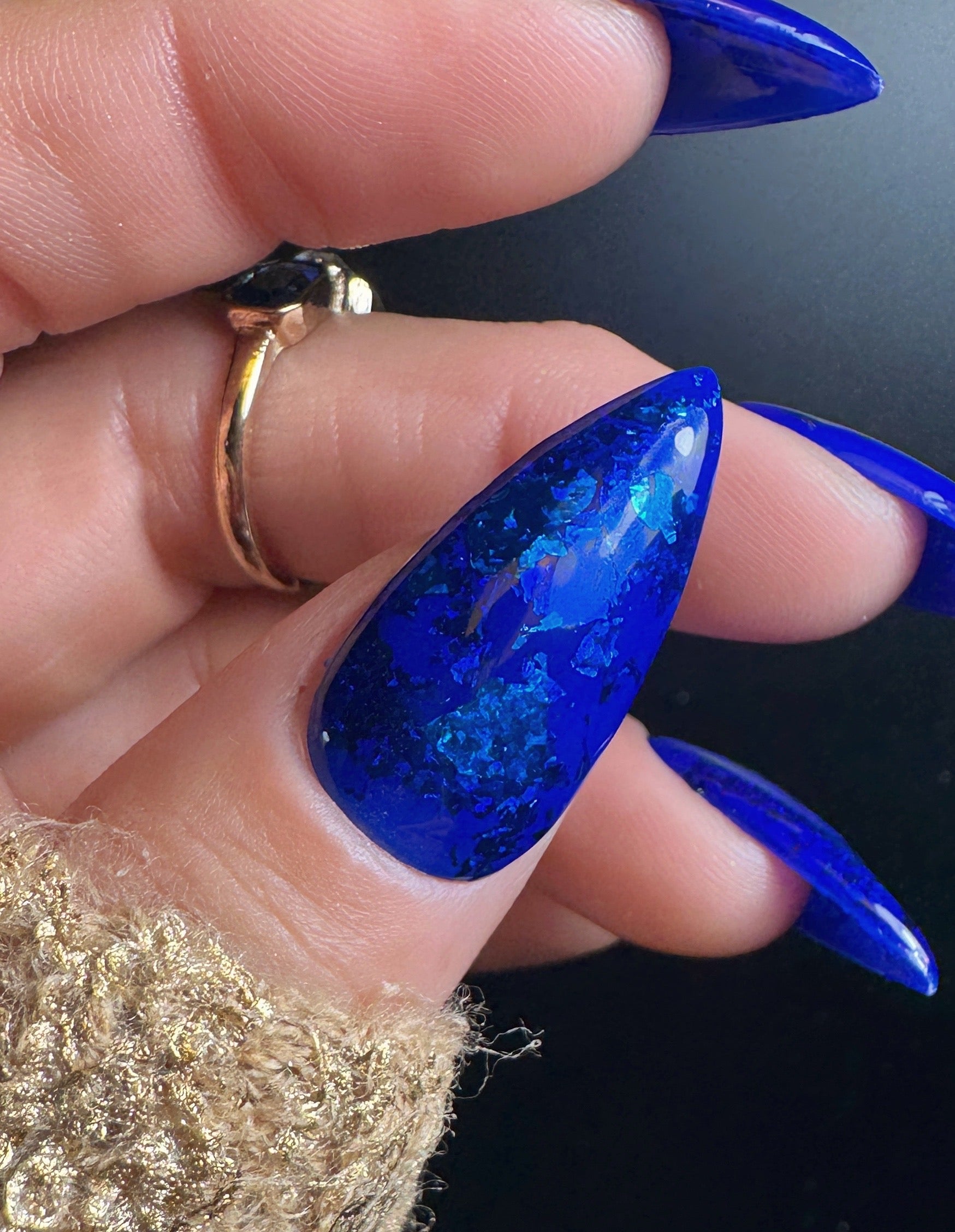 Hand with blue glitter nail design on a dark background