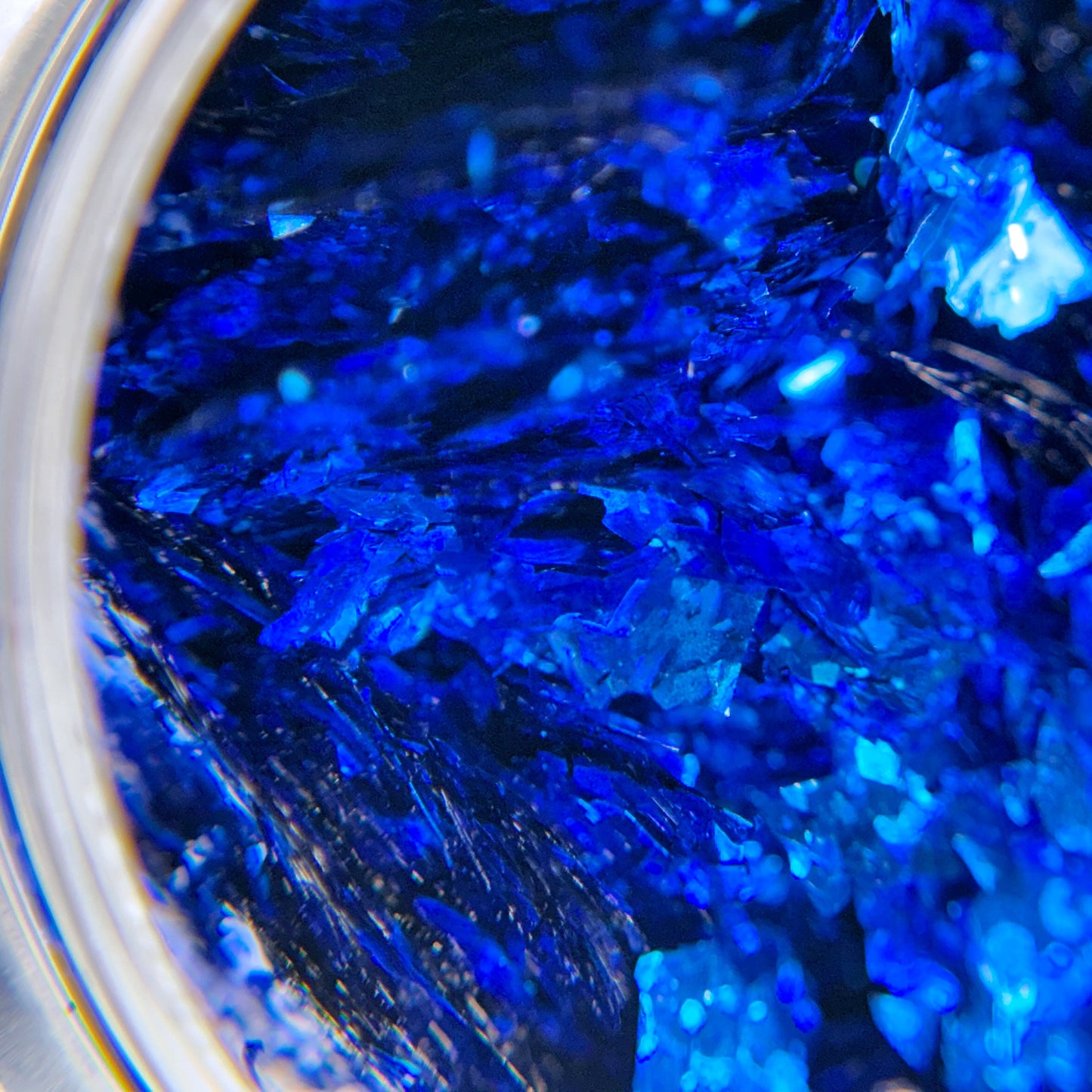 A close-up view of blue foil flake nail art glitter, showing the shiny, metallic surface and the flaky texture.