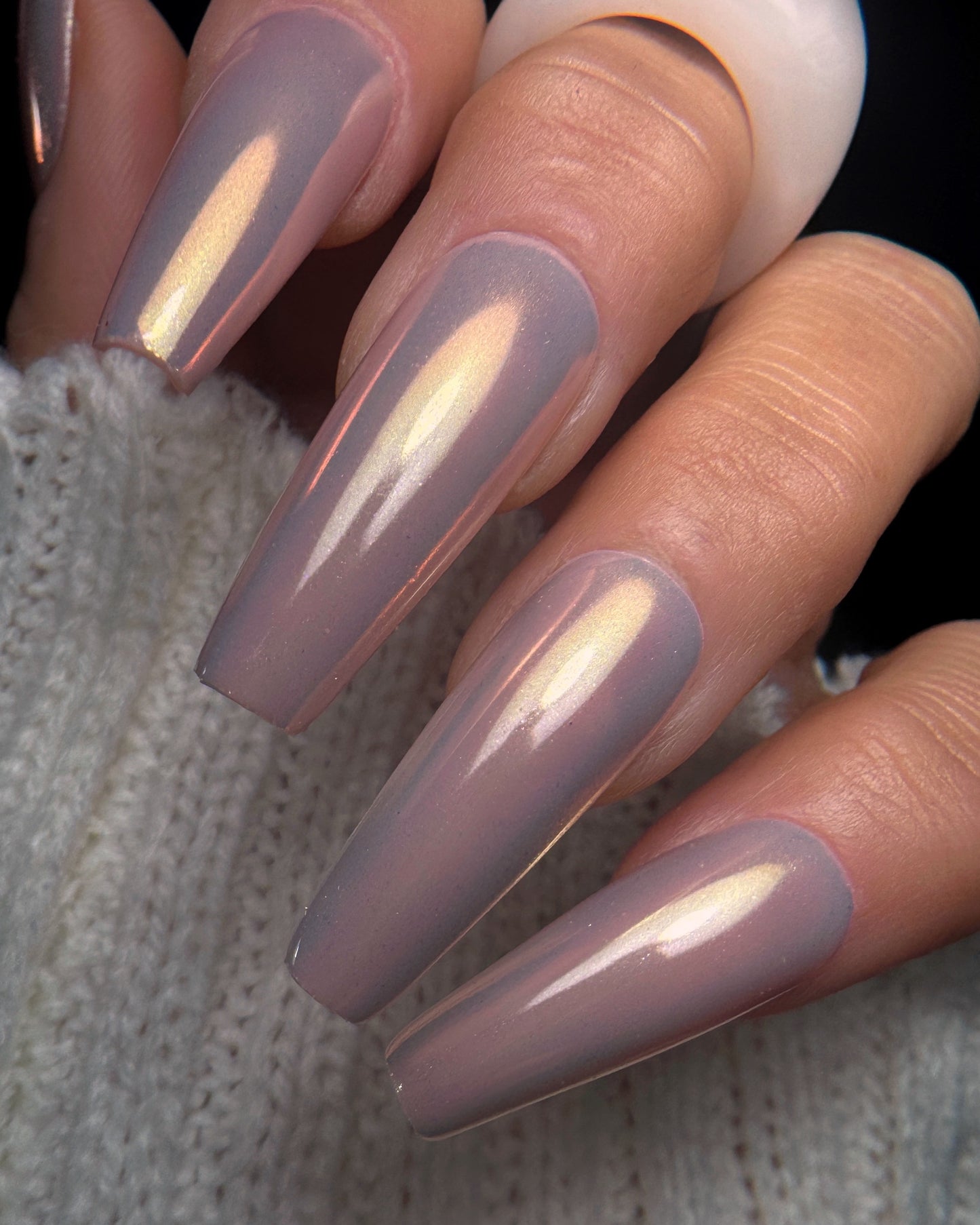 Manicured hand with long square nails on dark backdrop
