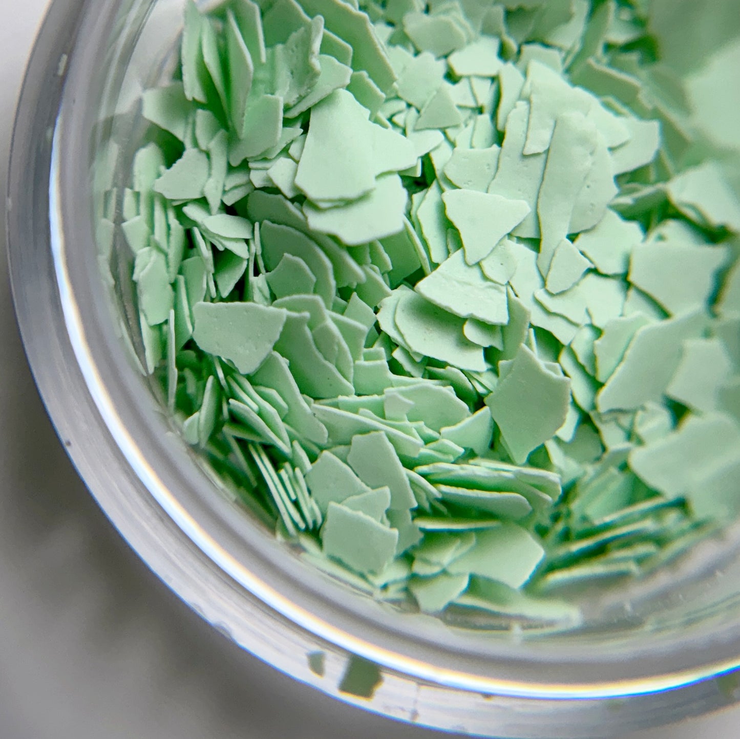 Close up of mint green flakes in jar intended for nail art.