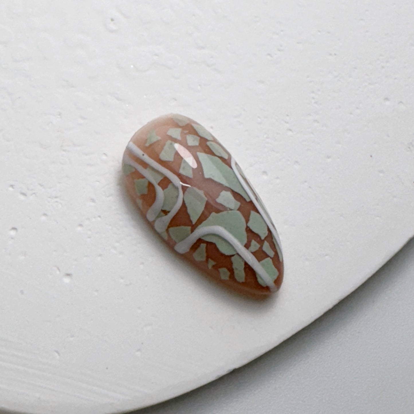 Decorated nail tip on white textured surface.