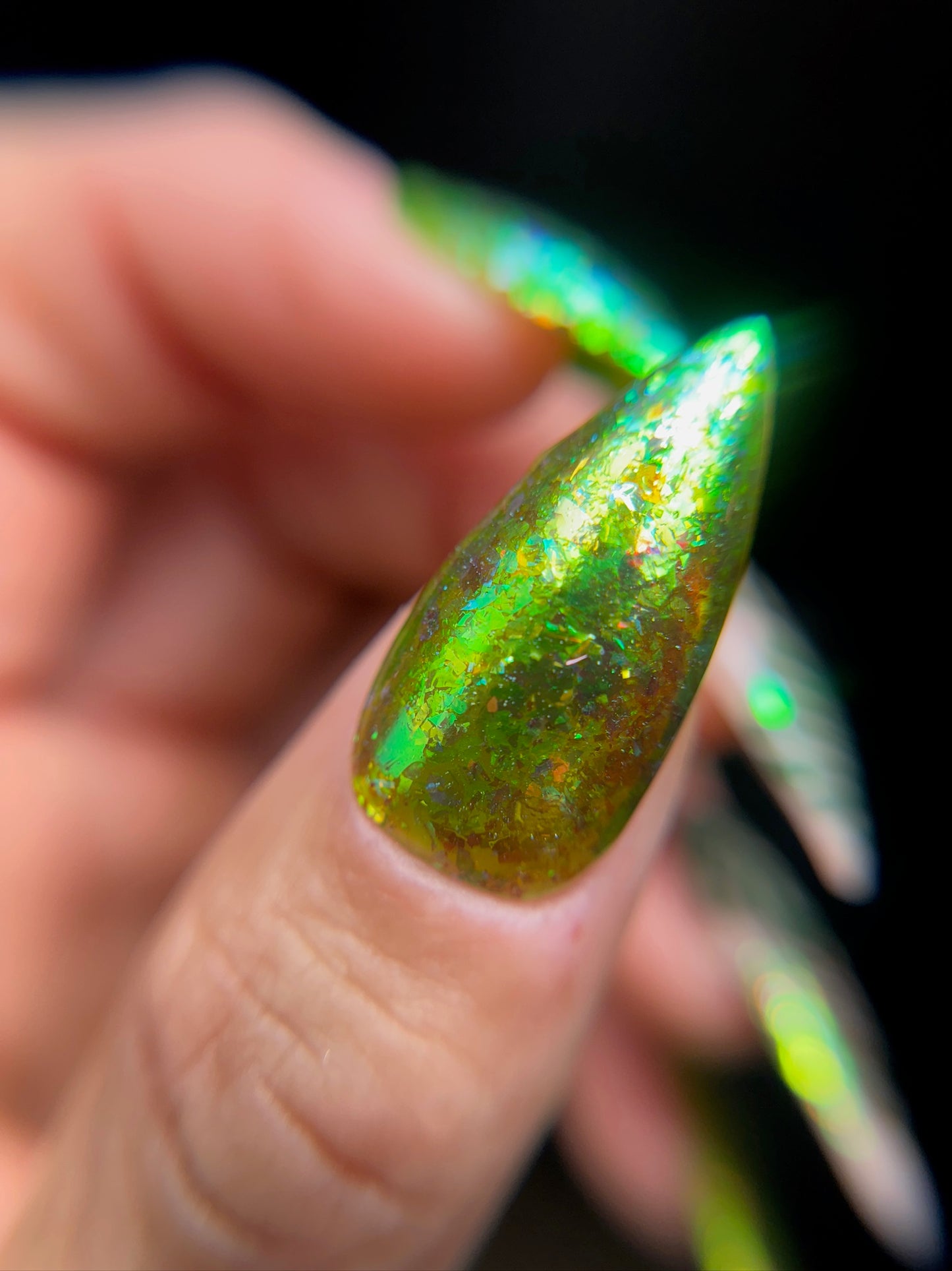 Close-up of a manicured hand with iridescent green nail design on a dark background