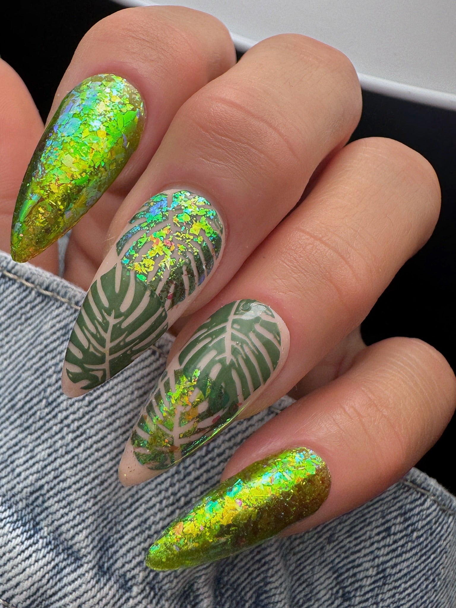 Nails with green and gold leaf design on a denim background