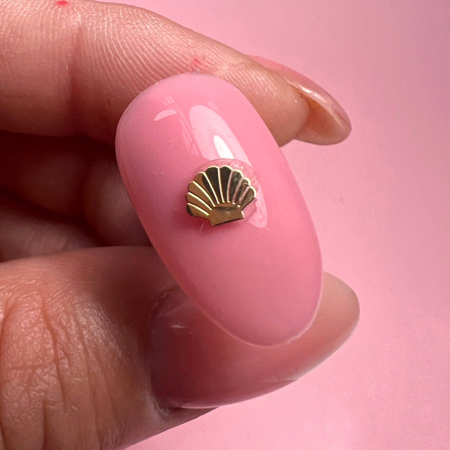 Close-up of a pink nail with a gold shell design on a pink background