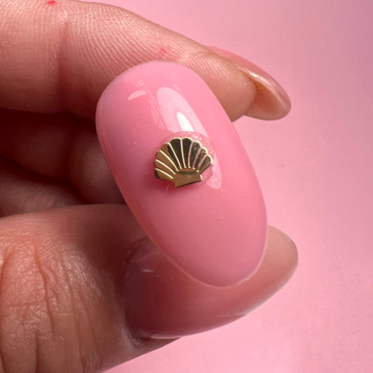 Close-up of a pink nail with a gold shell design on a pink background
