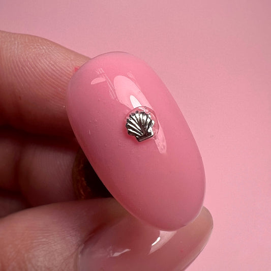 Pink nail with a silver shell charm held by a hand against a pink background