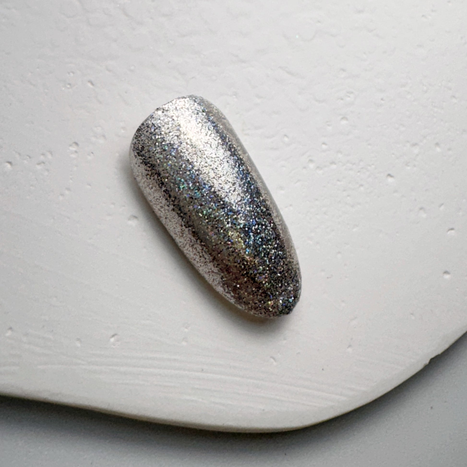 Glittery nail tip on white textured surface.