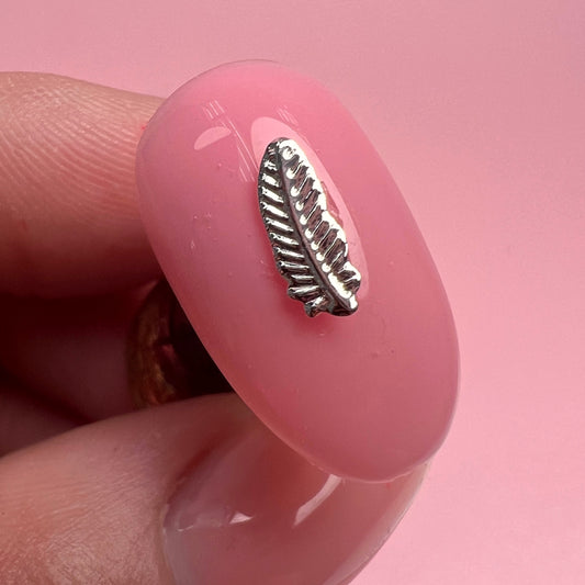 Pink nail with a silver feather charm against a pink background
