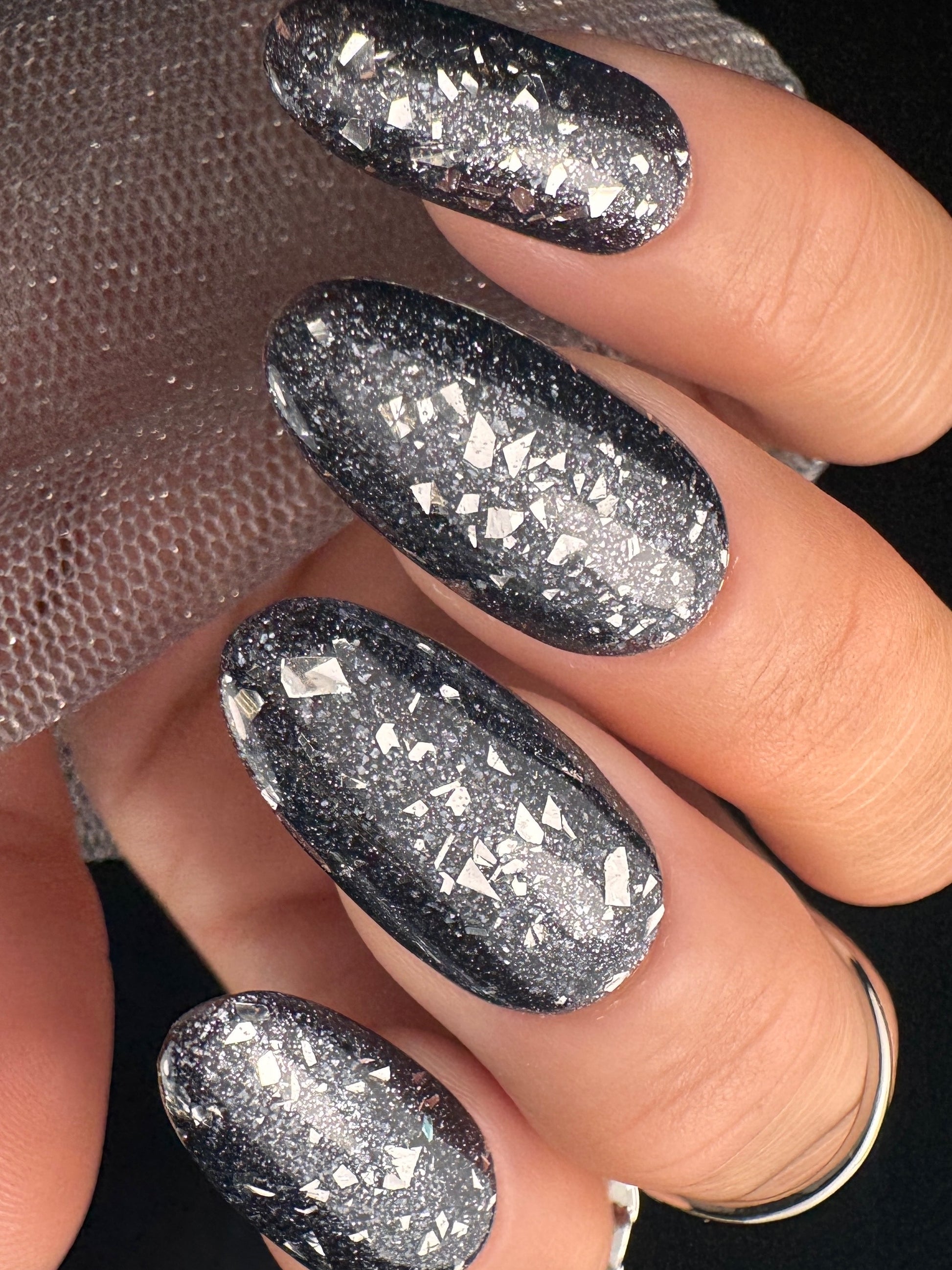Close-up of a hand with black glittery nail design on a dark background