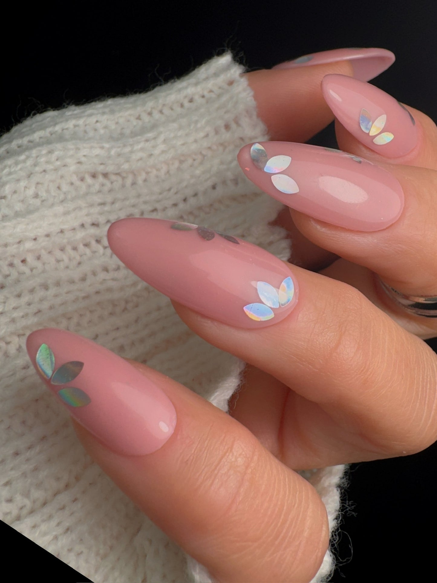 Close-up of a hand with pink nails featuring floral designs, wearing a white textured sweater.