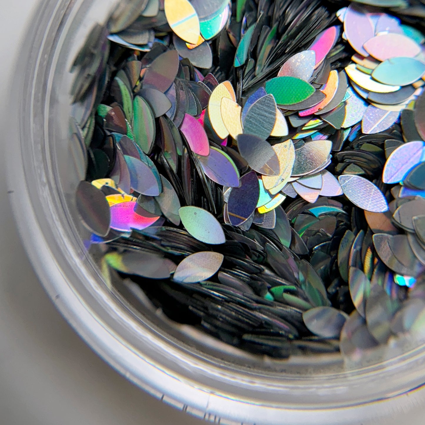 A close-up view of a container filled with silver holographic Dragon Scale Glitter intended for nail art.