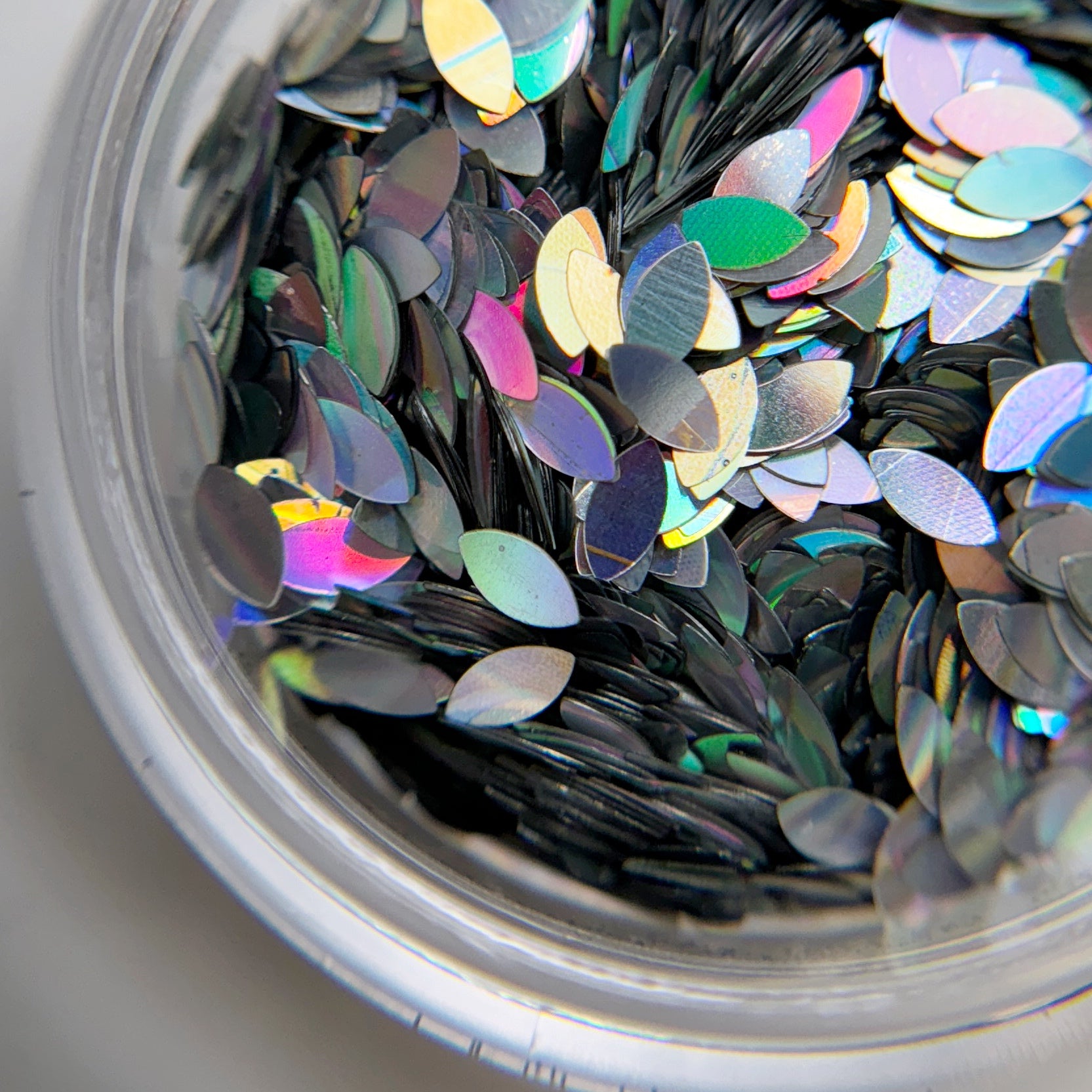 A close-up view of a container filled with silver holographic Dragon Scale Glitter intended for nail art.