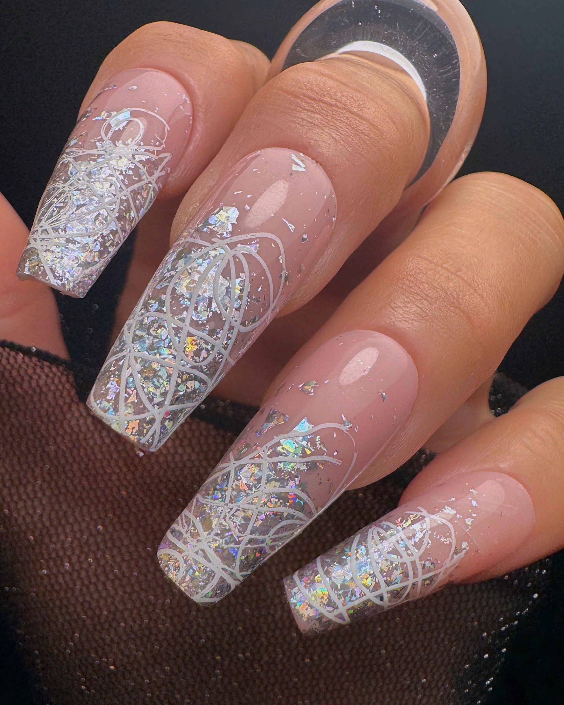 Nails with intricate white squiggle design over silver glitter on a neutral background