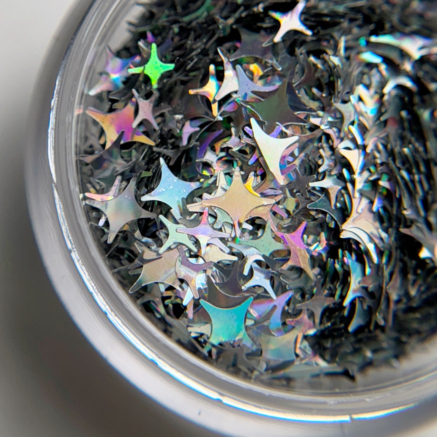 A close-up view of a jar containing silver holographic star-shaped glitter pieces.