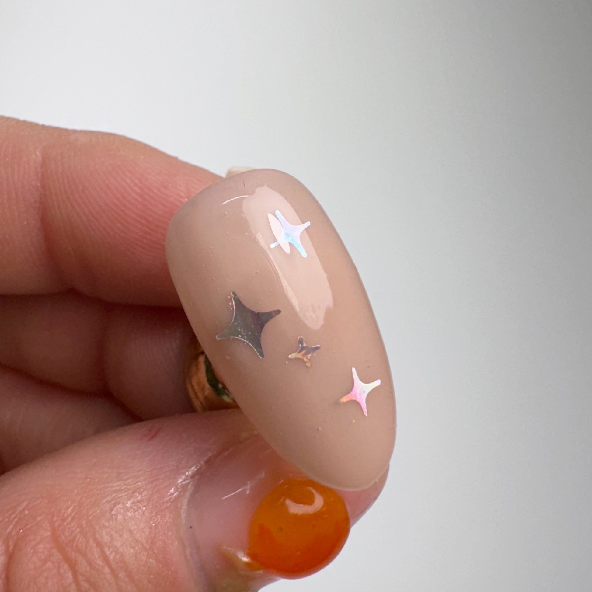 Hand holding decorated nail tip against light background.