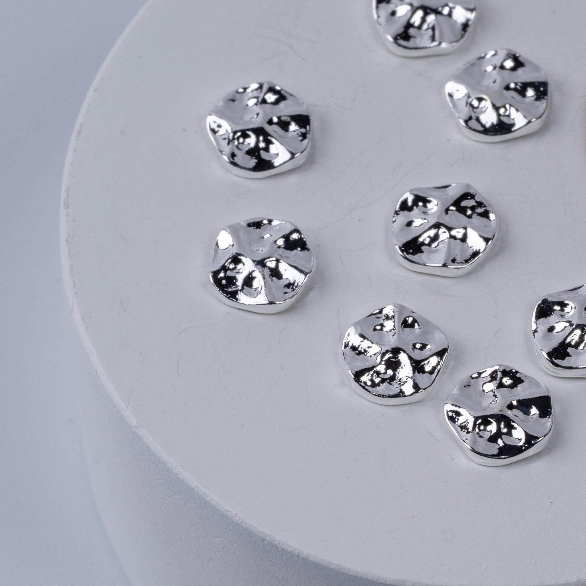 Silver nail charms on white circular base.