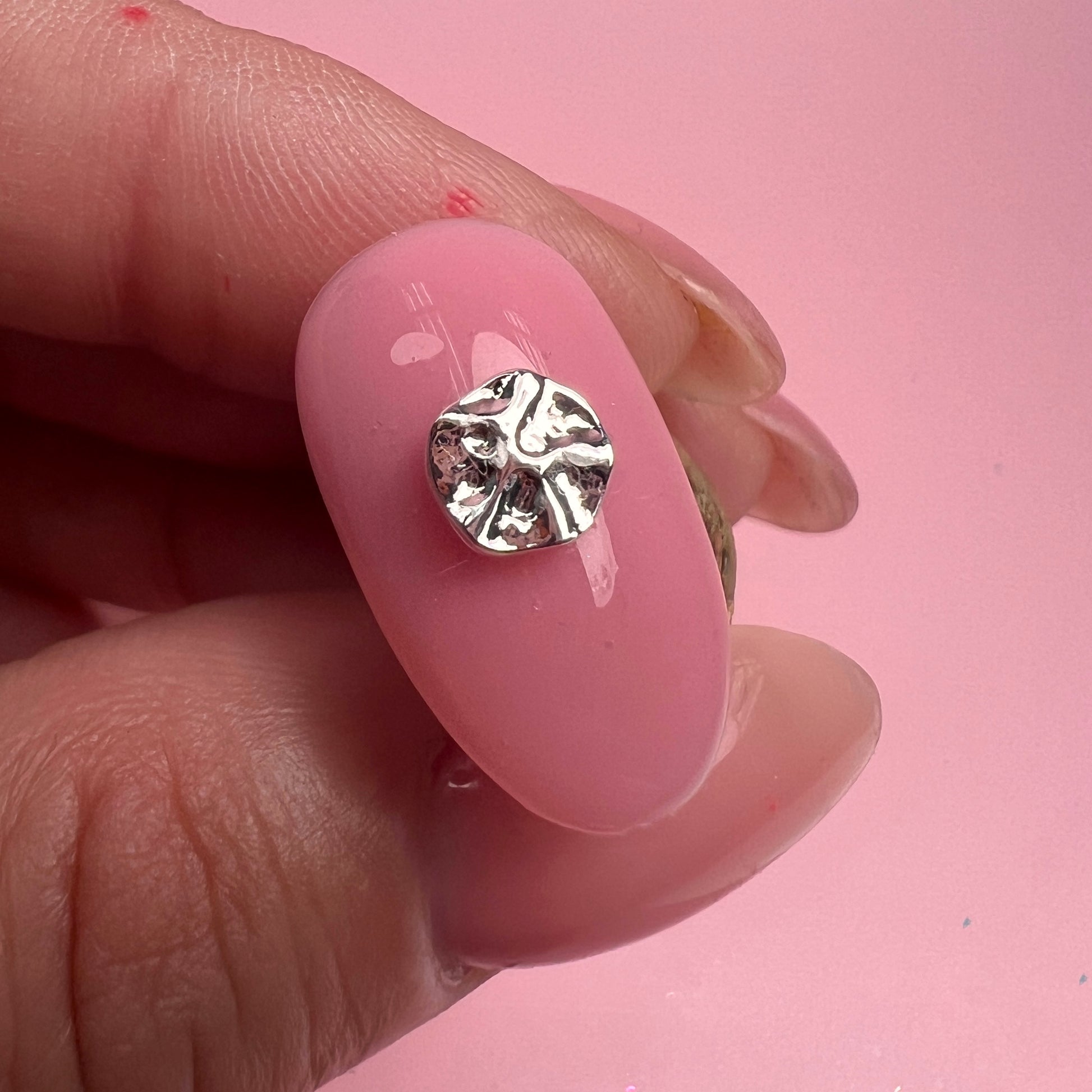 Silver nail art embellishment on a pink nail against a pink background