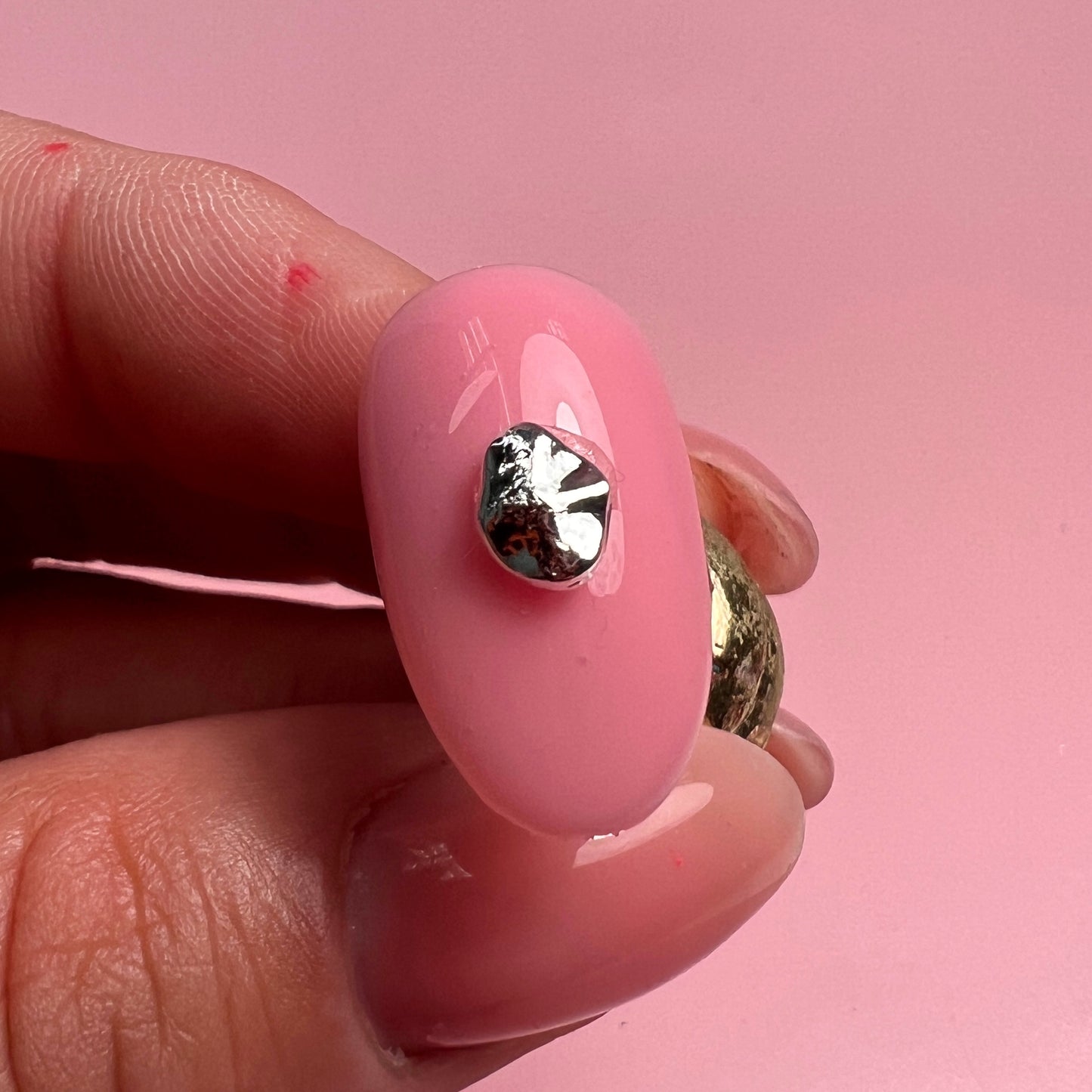 Pink nail with a silver charm on a pink background