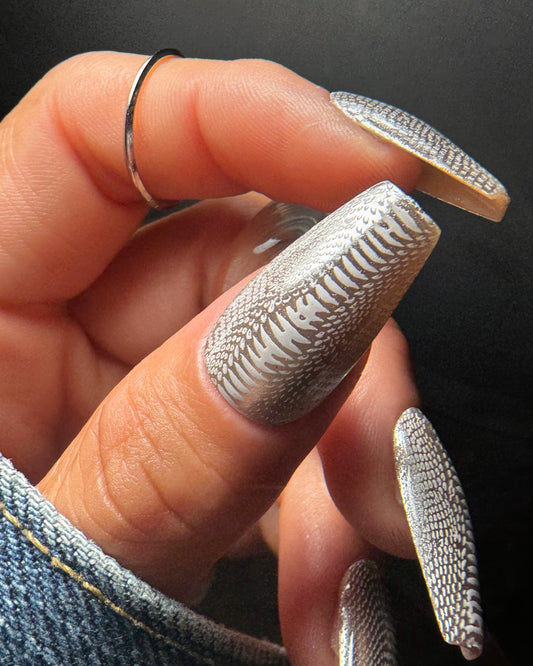 Hand with textured silver nail art against a dark background