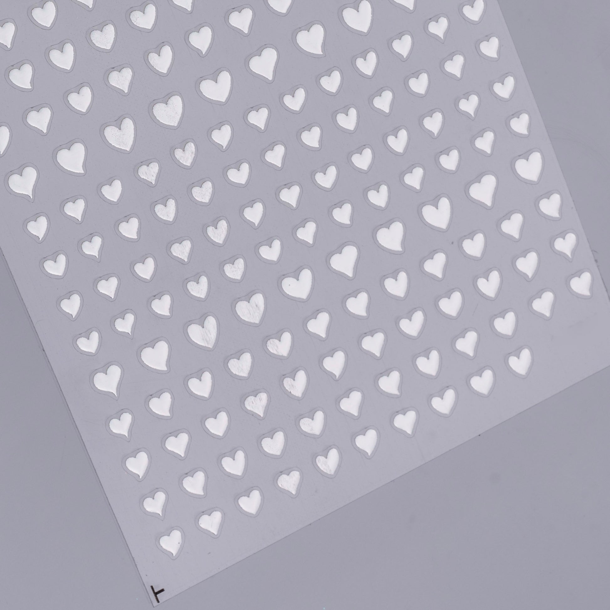 Sheet of silver heart-shaped stickers on a gray background