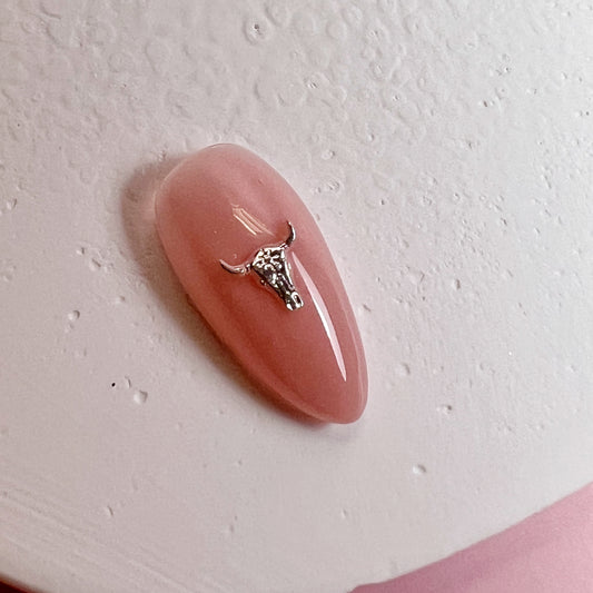 Pink nail with a small metallic charm on a light pink background
