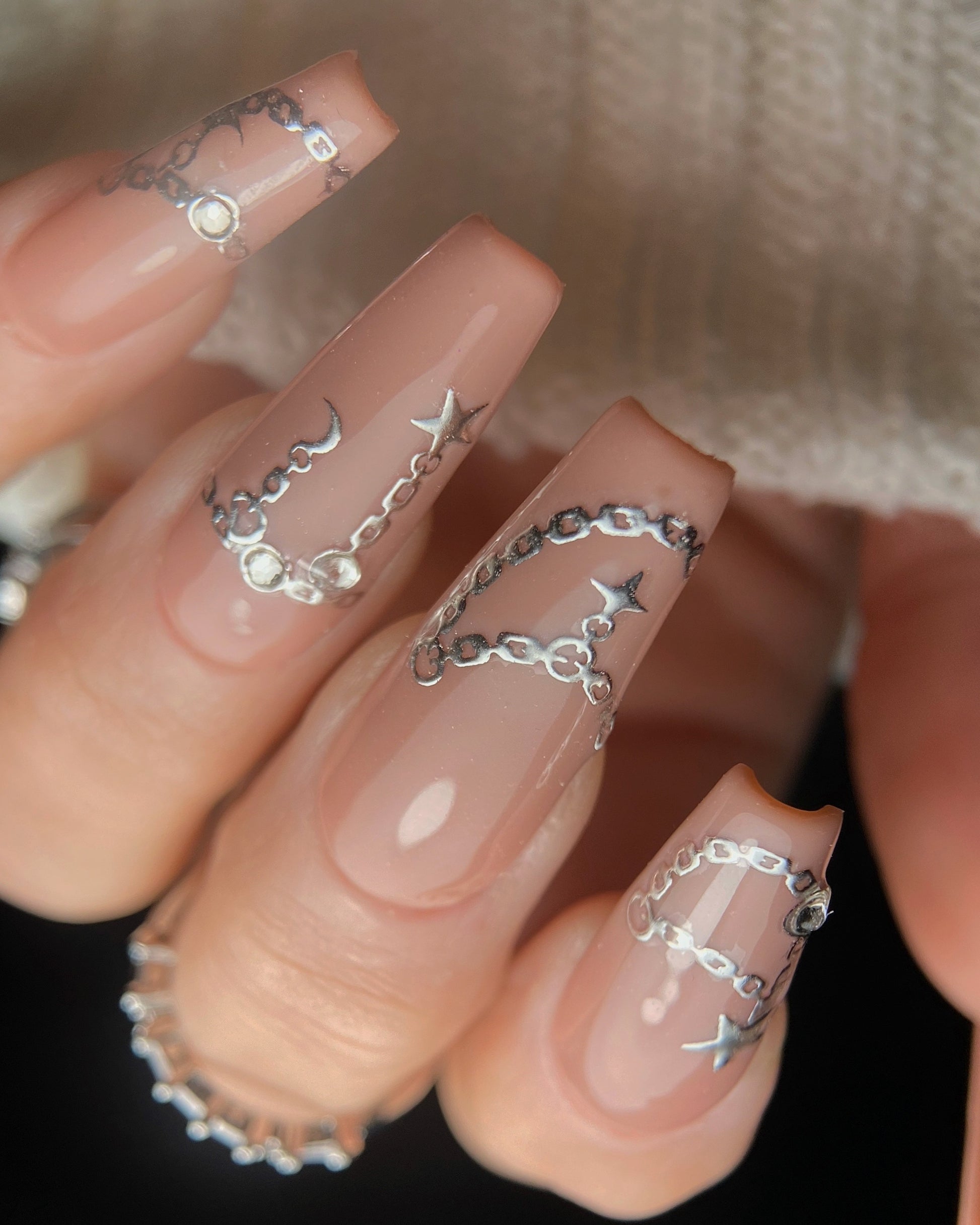 Nails with silver chain and star designs on a neutral background
