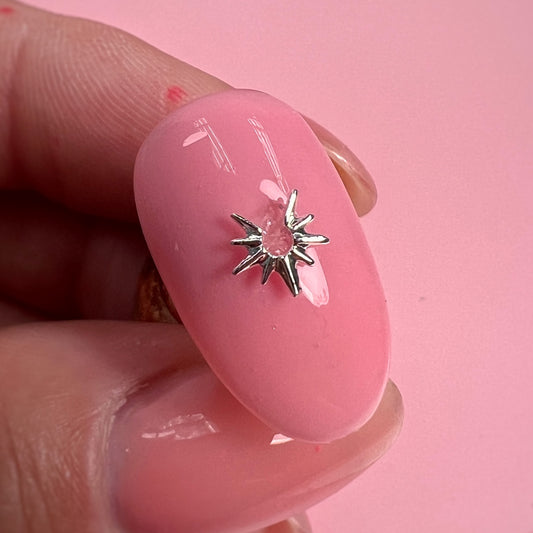 Pink nail with a silver star-shaped design held between fingers against a pink background