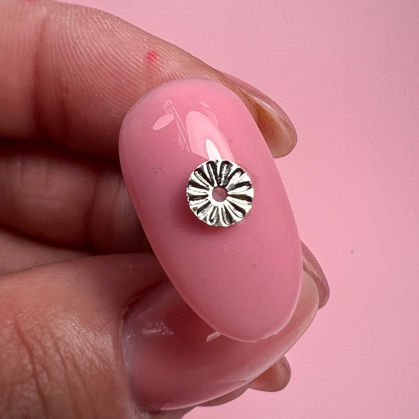 Silver round charm on a pink nail against a pink background
