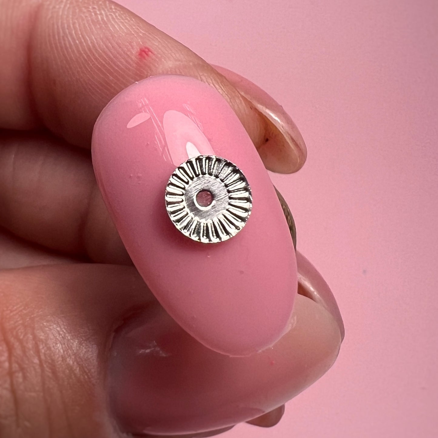 Silver metal bead on a pink nail against a pink background