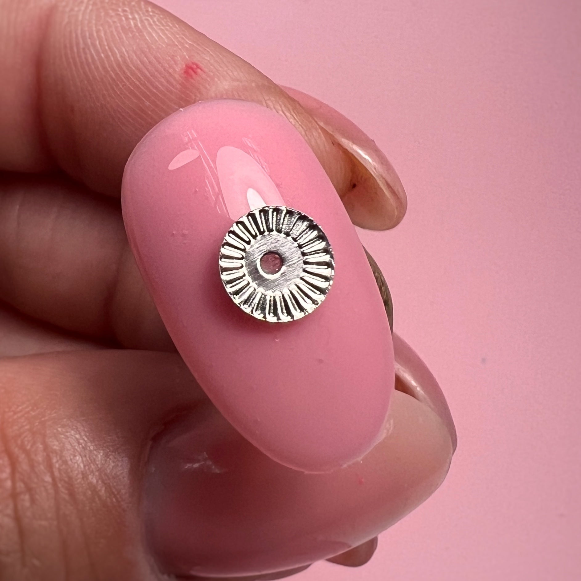 Silver metal bead on a pink nail against a pink background