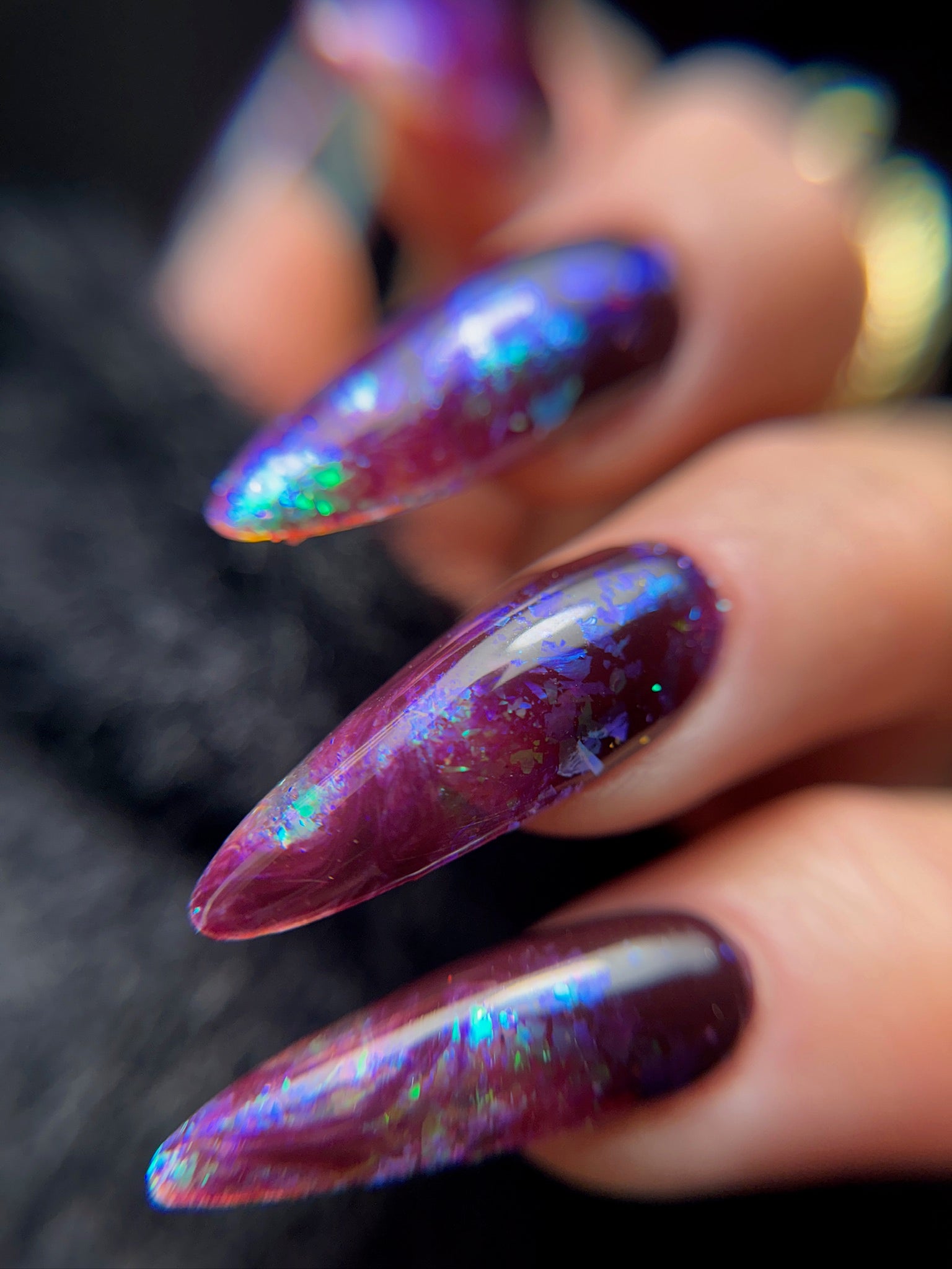 Close-up of a hand with iridescent purple nail design on a blurred background