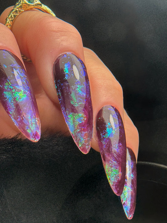 Iridescent purple and blue nail design on a dark background