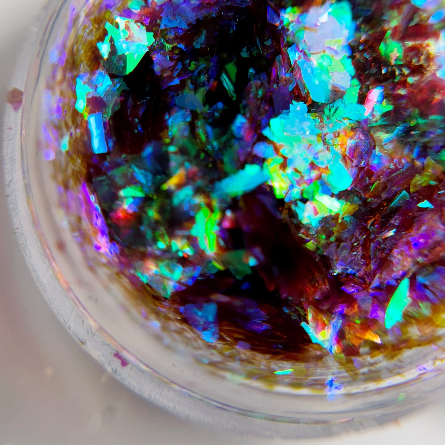 A close-up view of multicolored shimmering nail flakes inside a clear container.