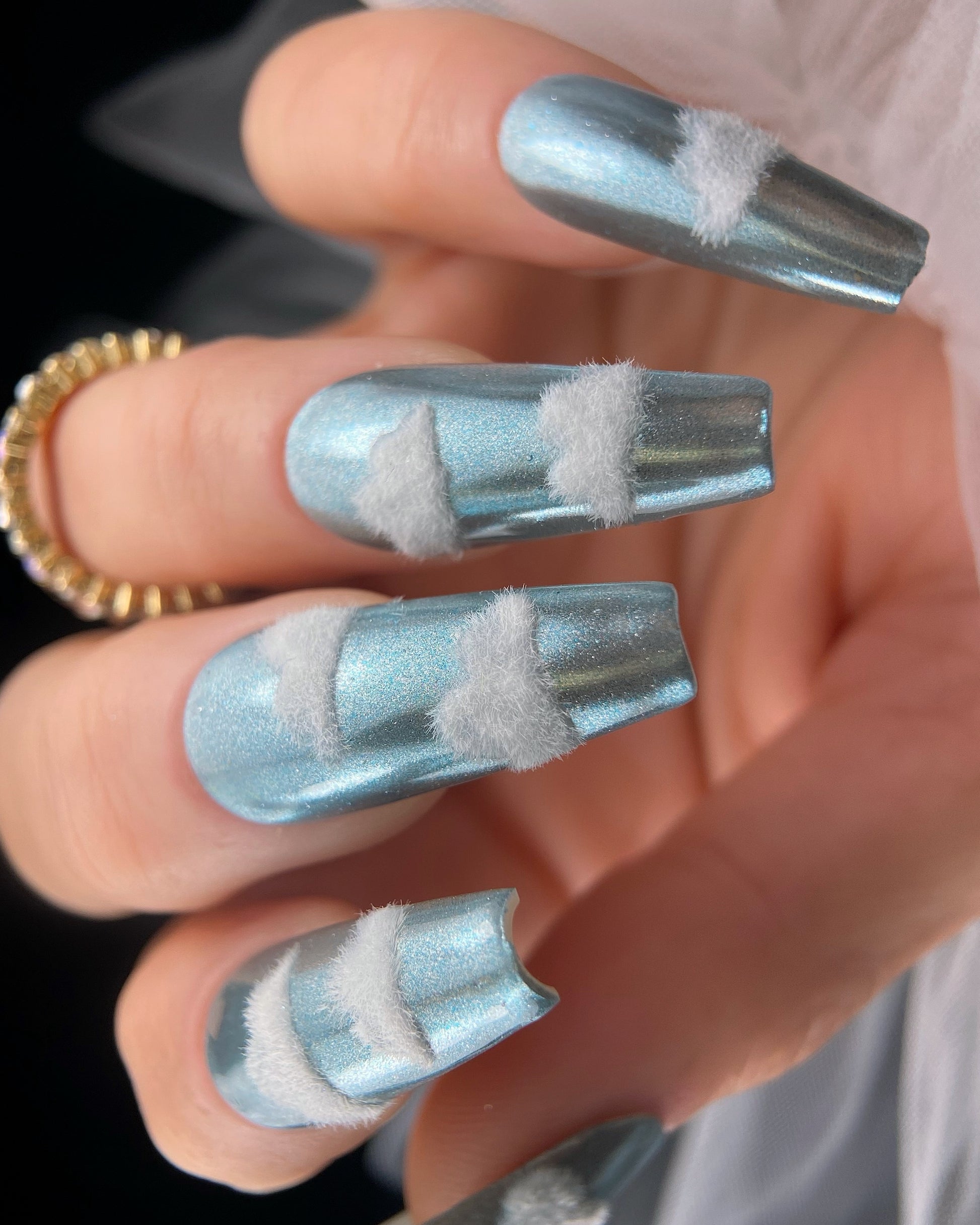 Nails with blue and white design held by a person wearing a gold ring.