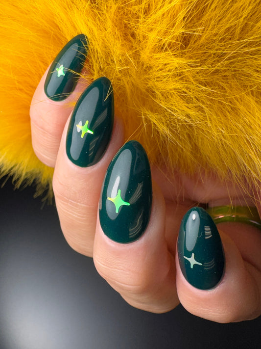 Hand with dark green nail polish featuring iridescent lime green star designs against a yellow fur background