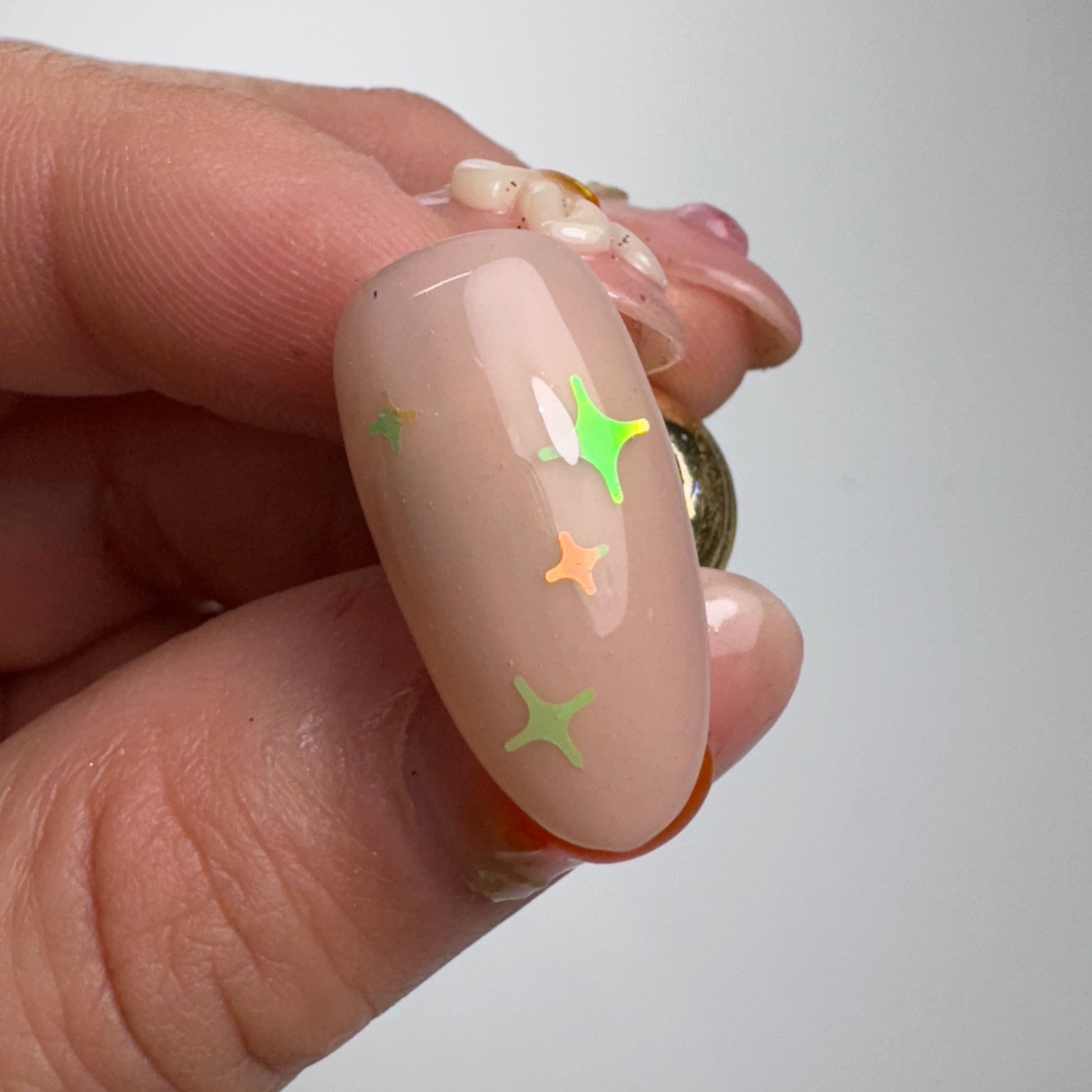 Hand holding decorated nail tip against light background.