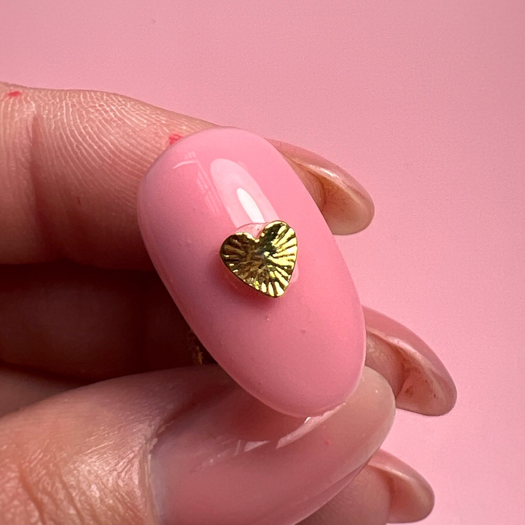Pink nail with a gold heart-shaped design on a pink background