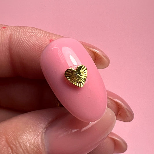 Pink nail with a gold heart-shaped design on a pink background