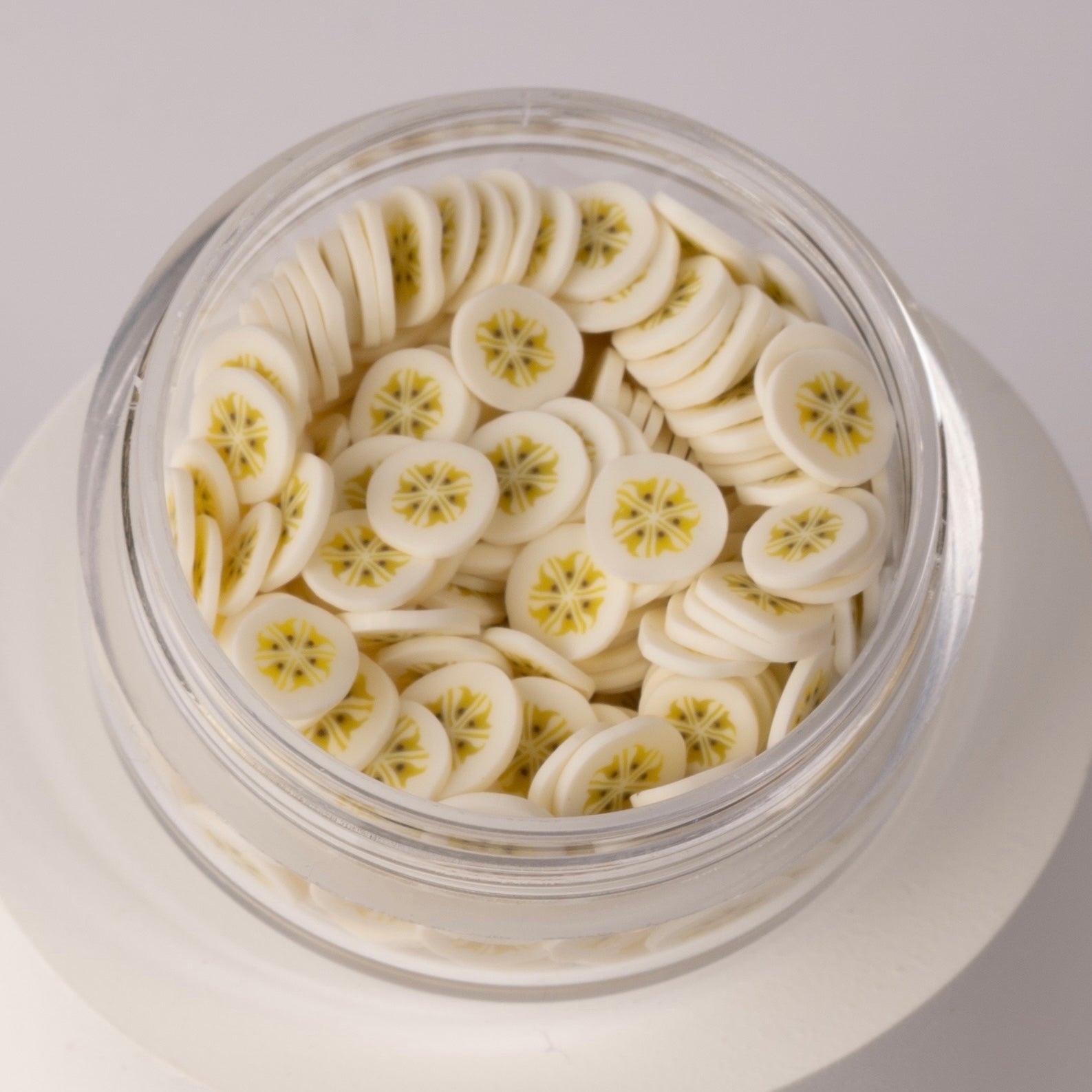Mini decorative banana slices in clear jar on white background.