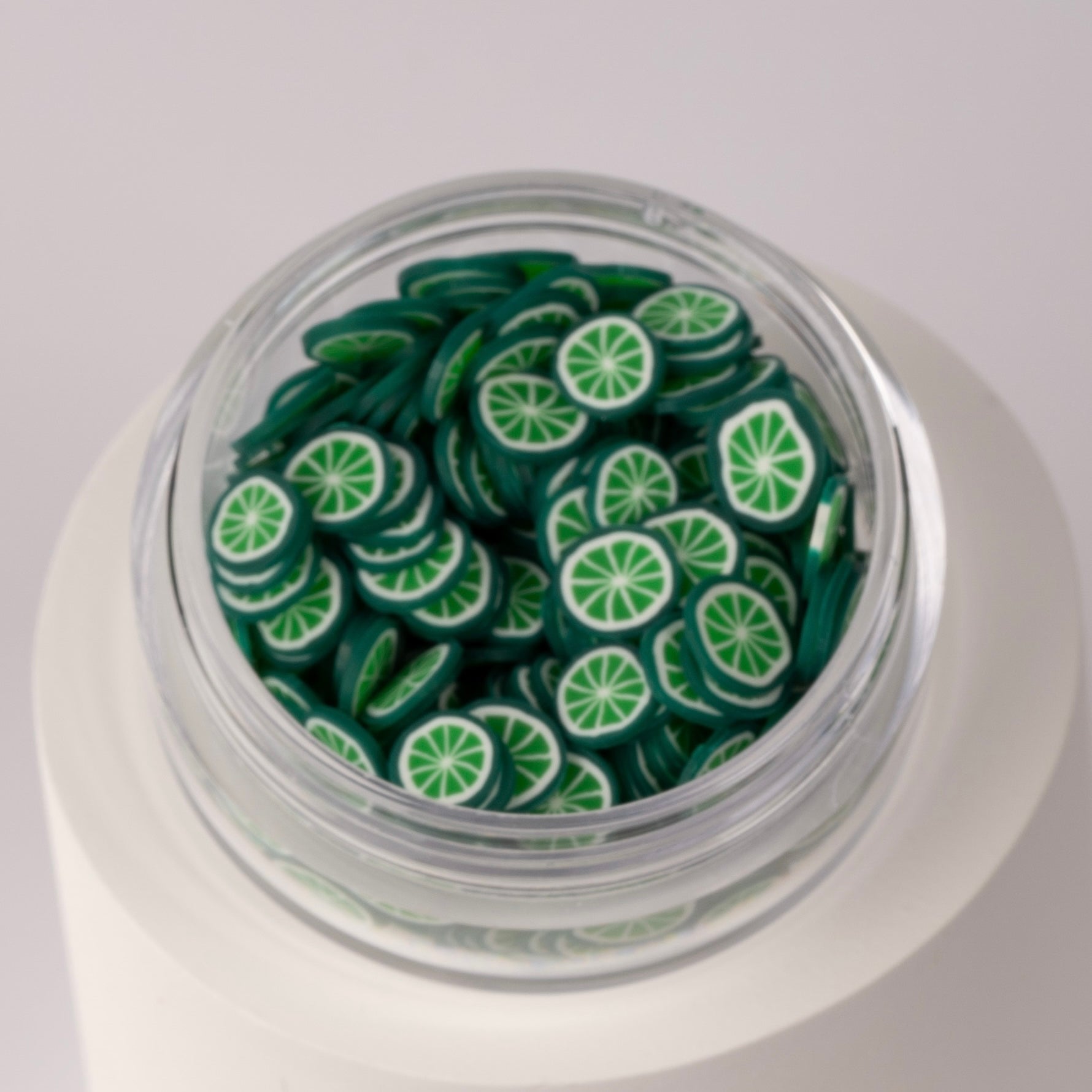 Mini decorative lime slices in clear jar on white background.