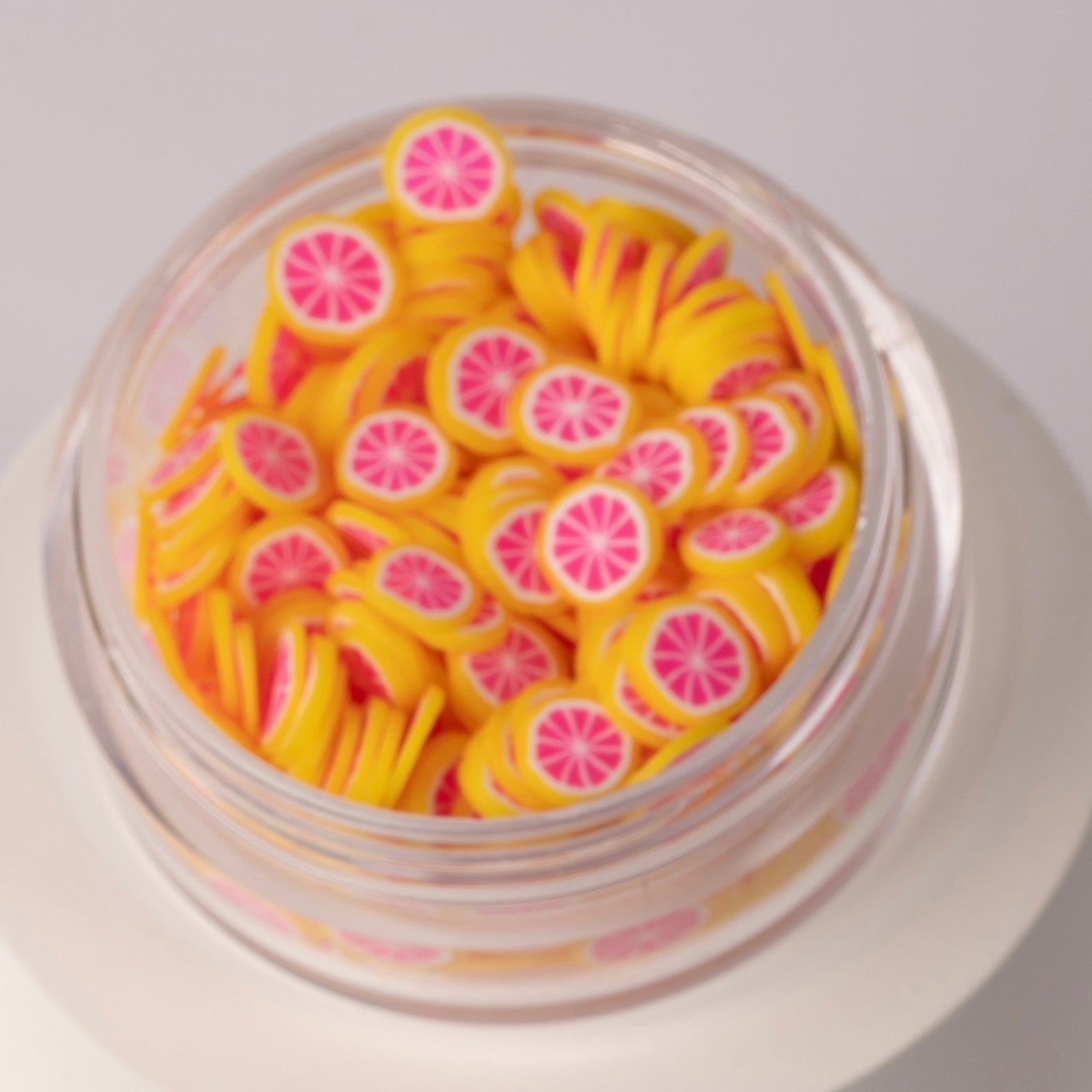 Mini decorative grapefruit slices in clear jar on white background.